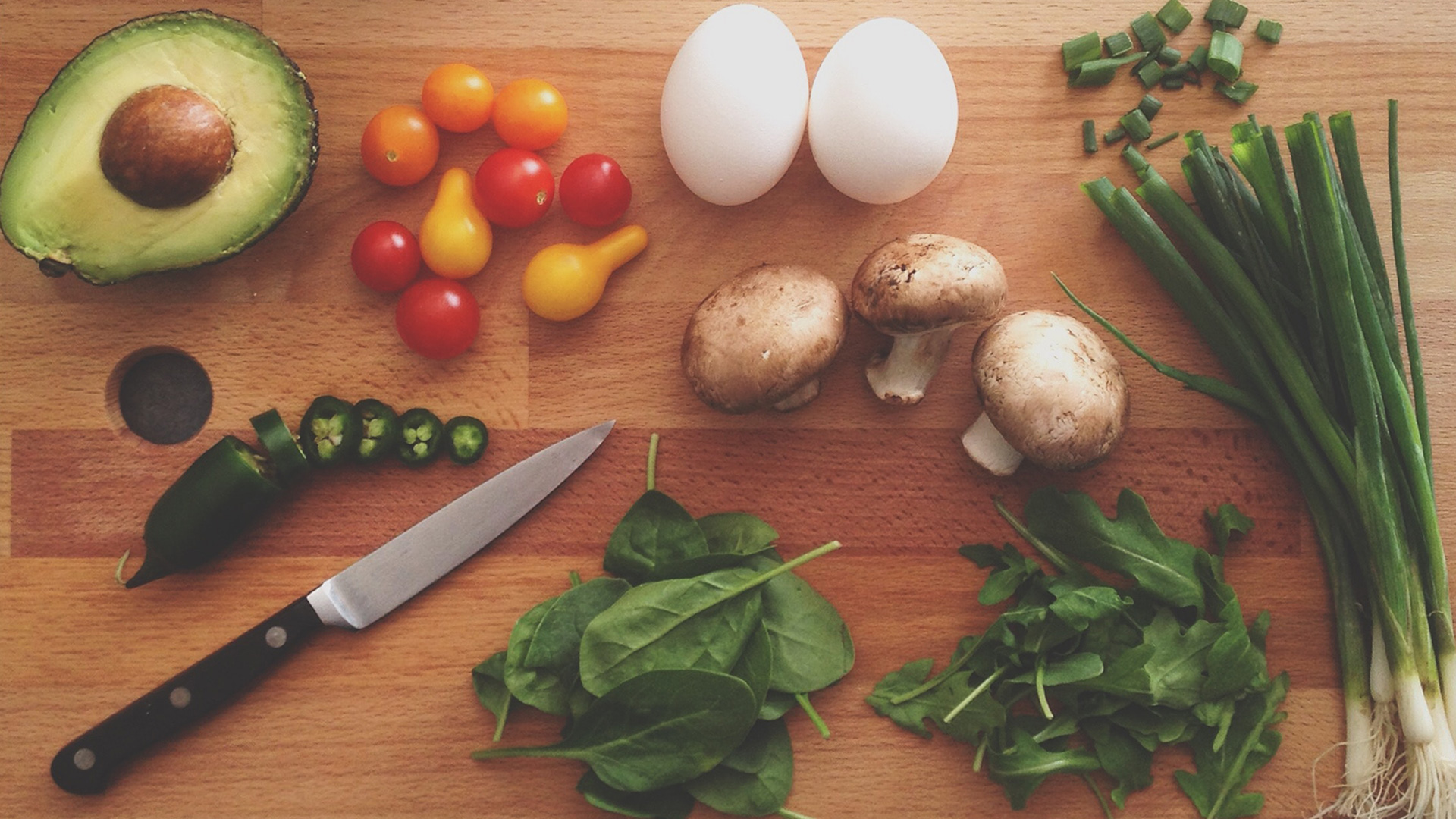 A chopping board with vegetables, herbs and a knife