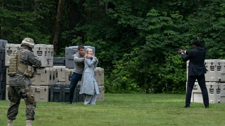 A man holds a gun to a woman in a standoff with armed guards