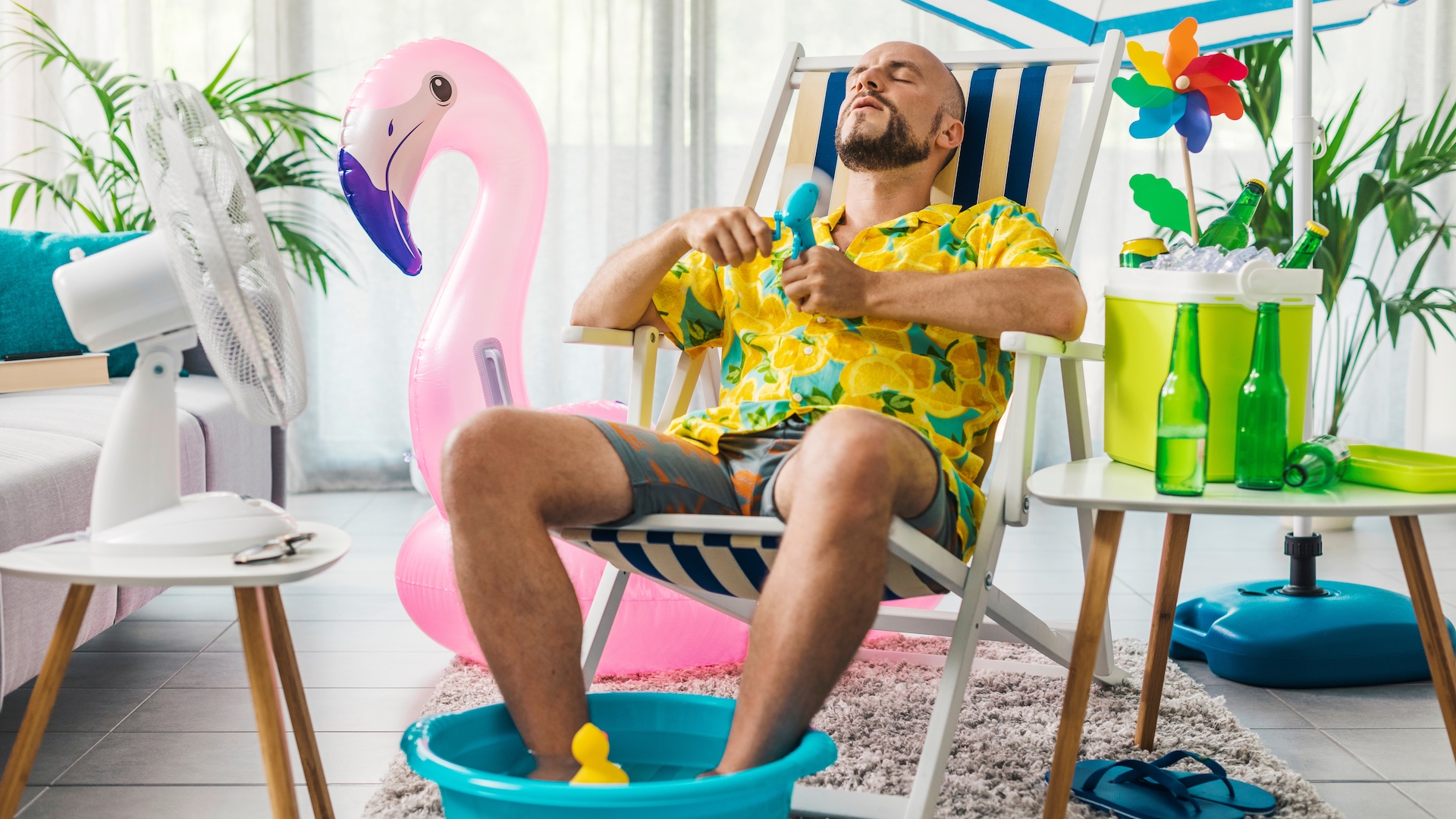 Man spending summer vacations at home, he is cooling himself with electric fans and sitting on a deckchair