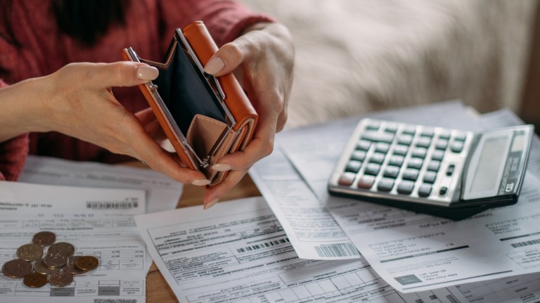 Close-up of woman's hands with empty wallet and utility bills.Many utility bills, coins and hands in a warm sweater holding an open wallet;