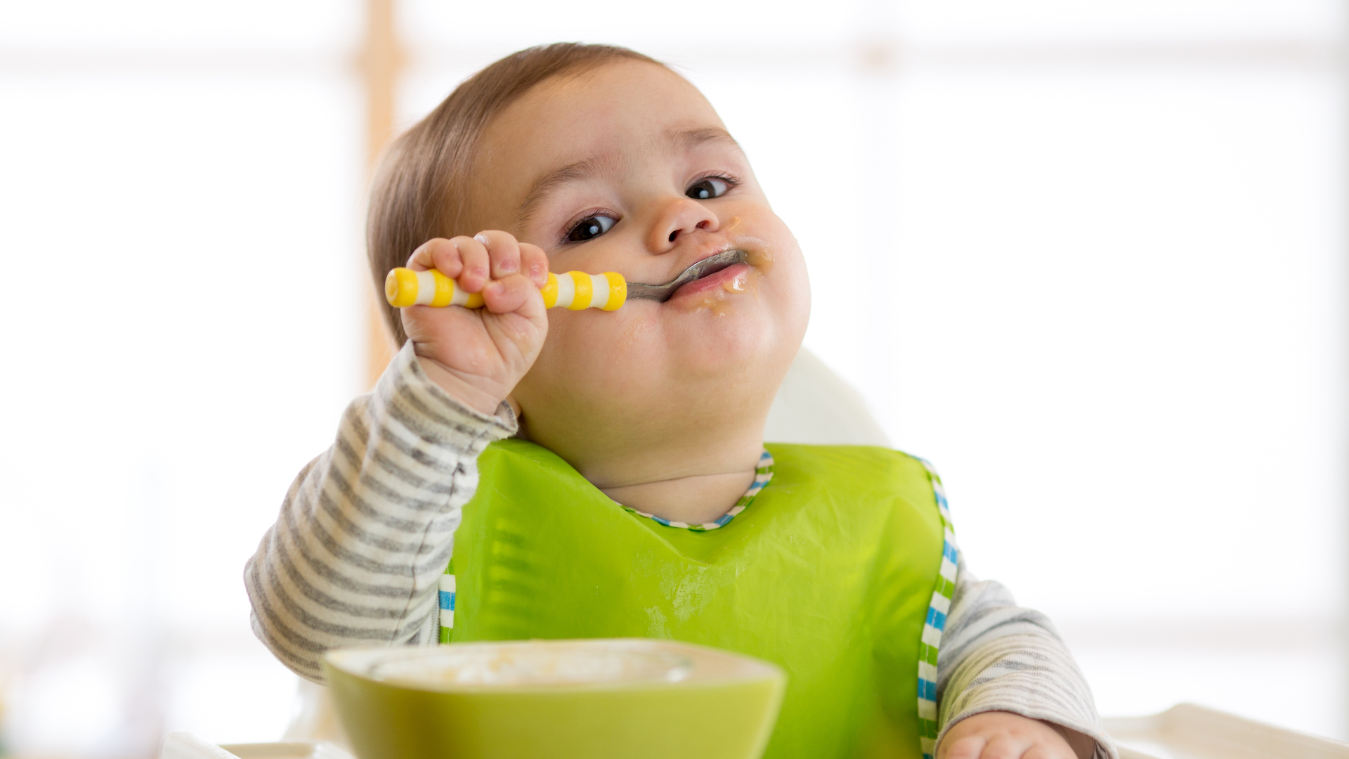 Happy infant baby boy spoon eats itself;