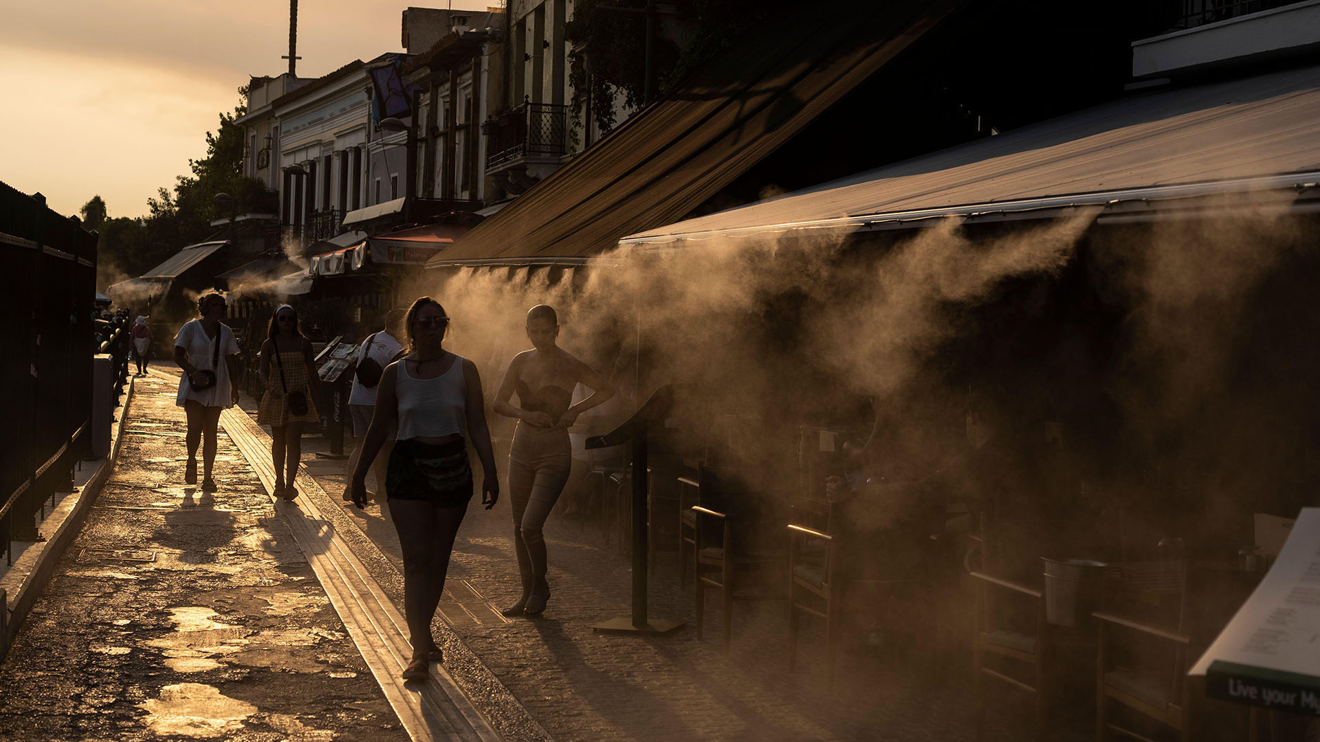 People walk next a mist machine to cool down, in Monastiraki district of Athens