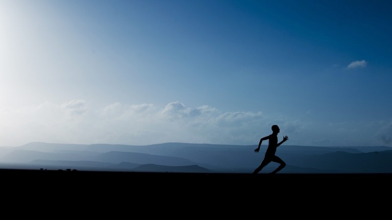 Silhouette of a man running with sky and mountains in the background