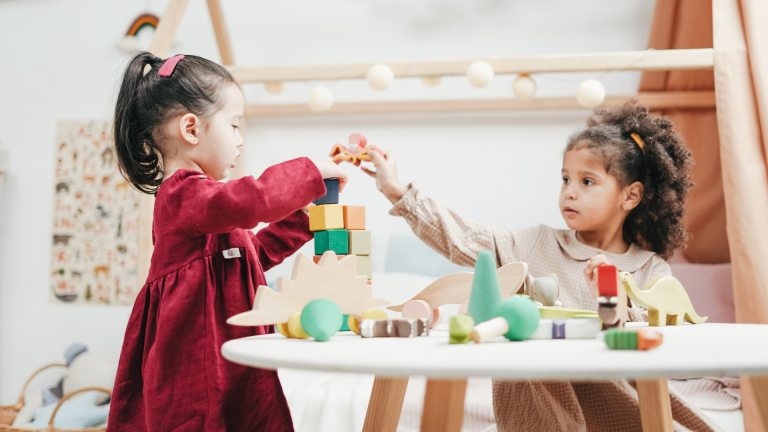 Two girls play with wooden blocks in a childcare setting