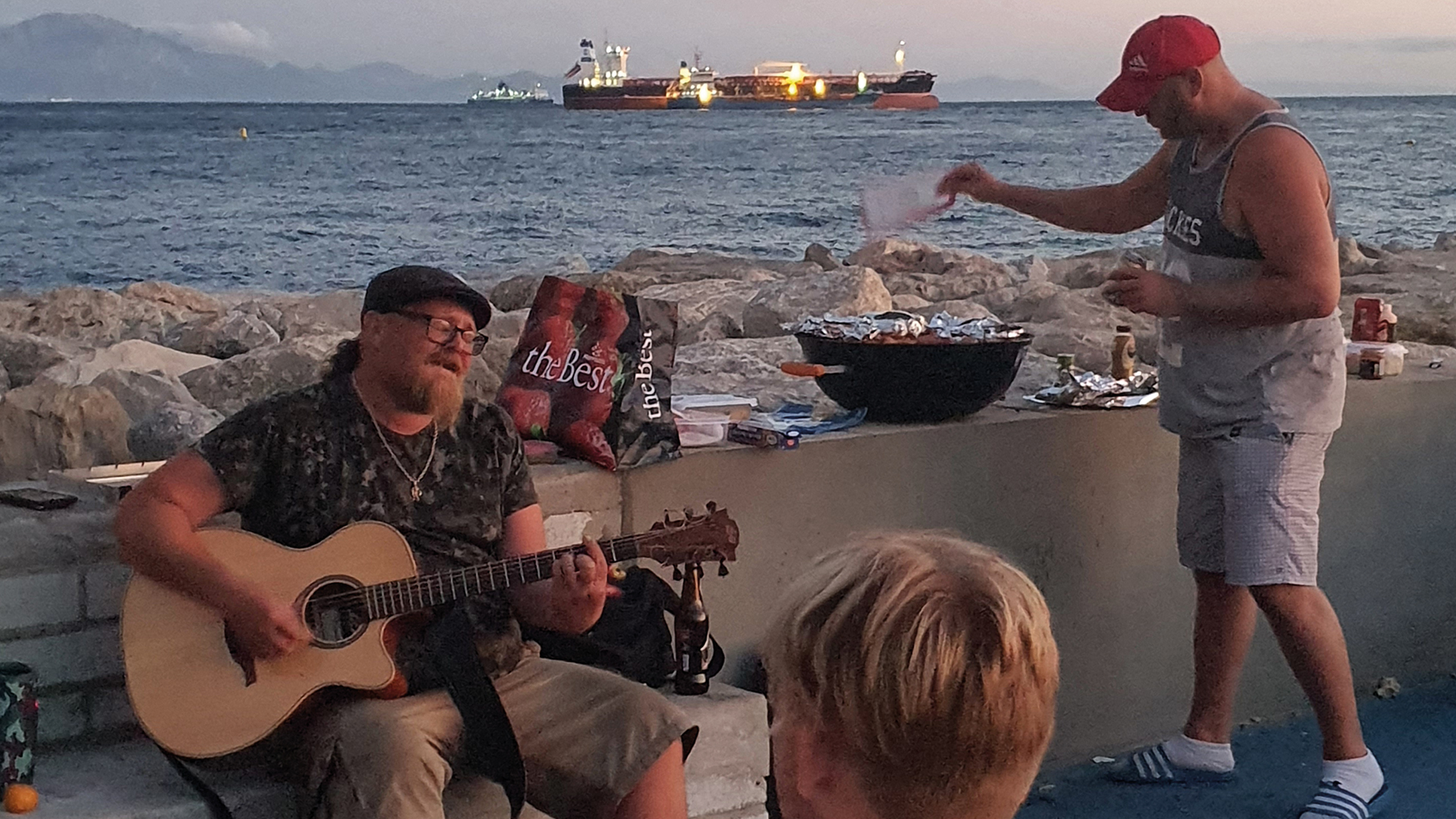 Stephen Woodhouse playing guitar on the beach to an audience