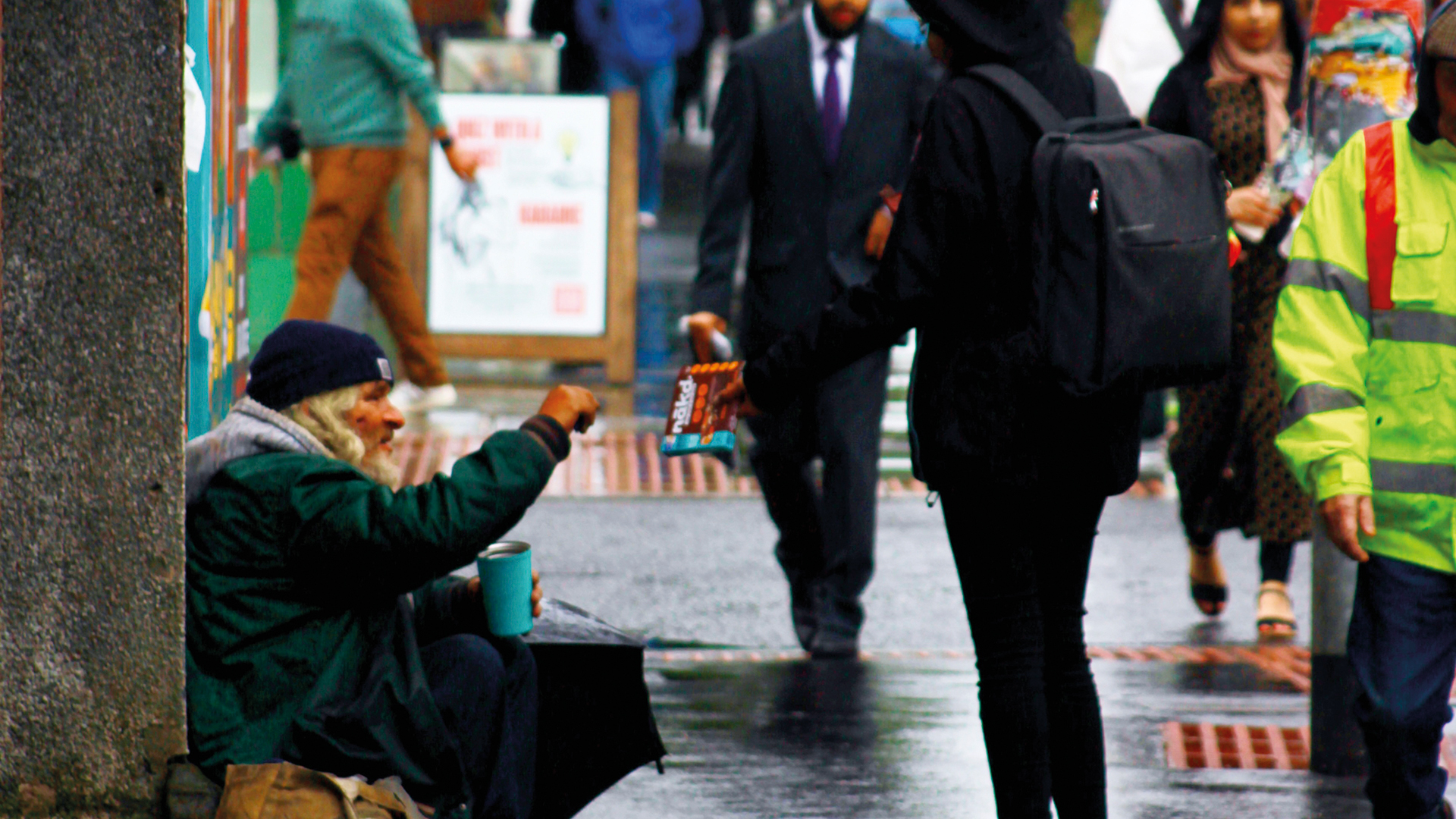 A man sits on the pavement taking food offered