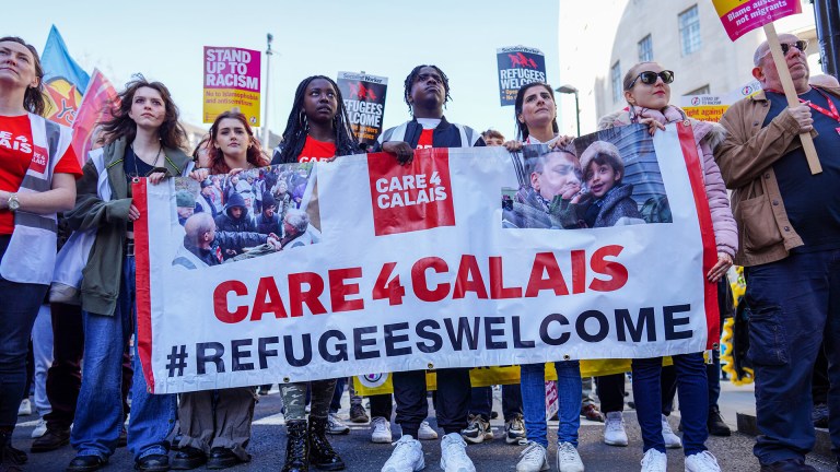 People marching and holding a Care4Calais banner that says refugees welcome