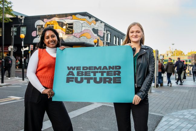 Two women hold a banner reading 