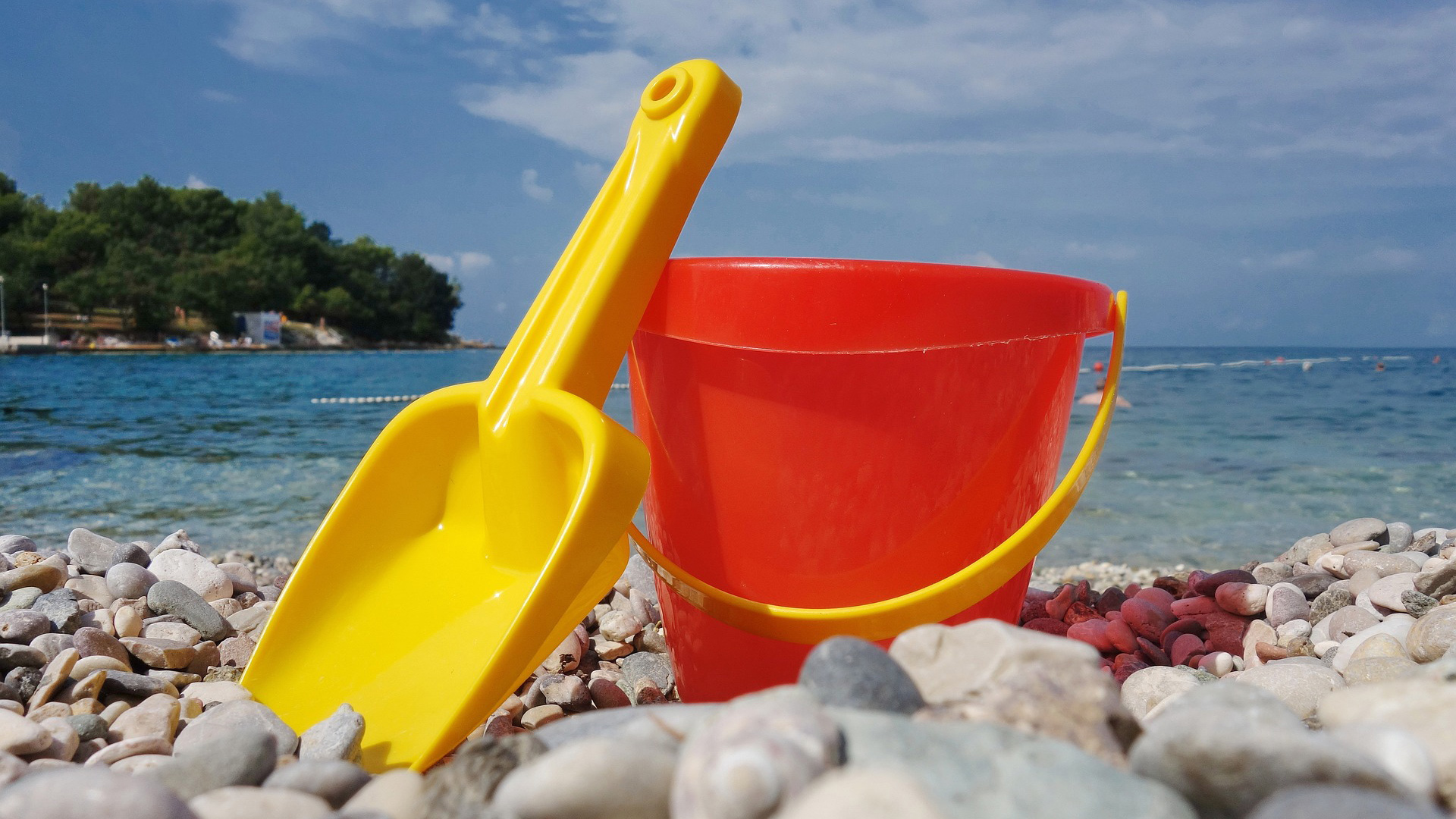 A yellow spade and red bucket on a pebble beach