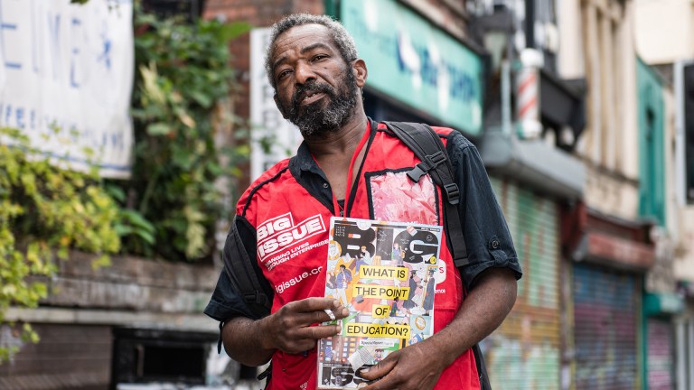 Big Issue vendor Jeff Knight in his red tabard carrying a copy of the magazine
