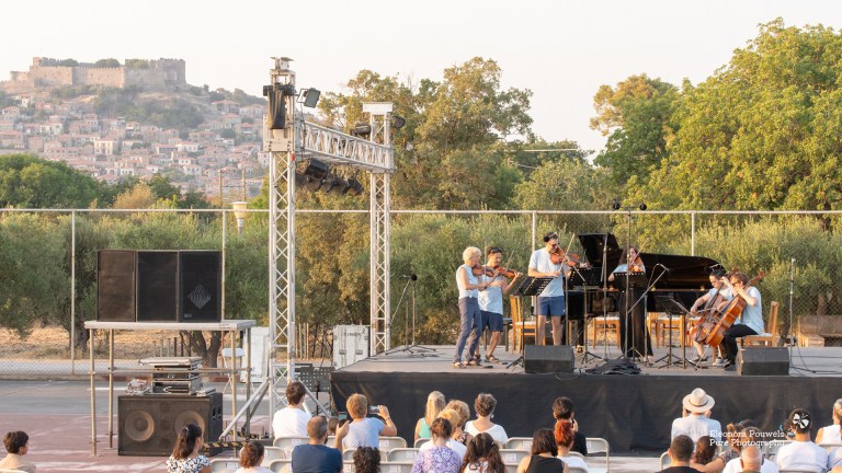 People sit watching classical musicians on an outdoor stage