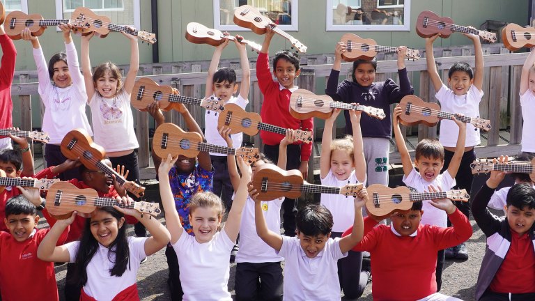 Pupils at Hallsville Primary School, Canning Town, holding ukeleles in the air to celebrate their music education grant
