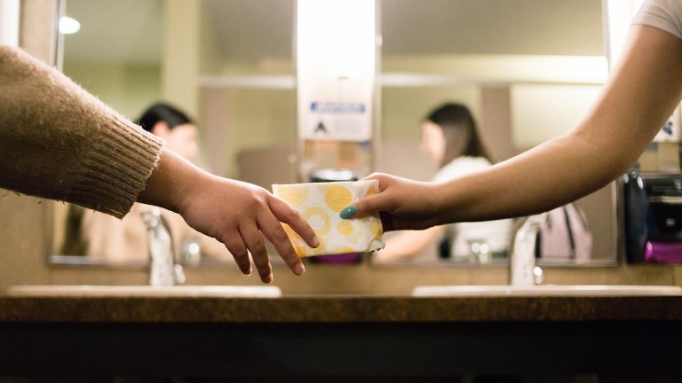 Women in a bathroom sharing menstrual products