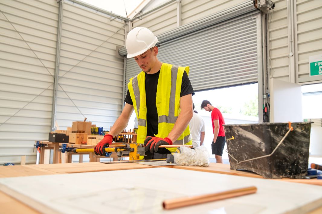 A young man in high-vis and a hard hat learning construction skills in a workshop setting