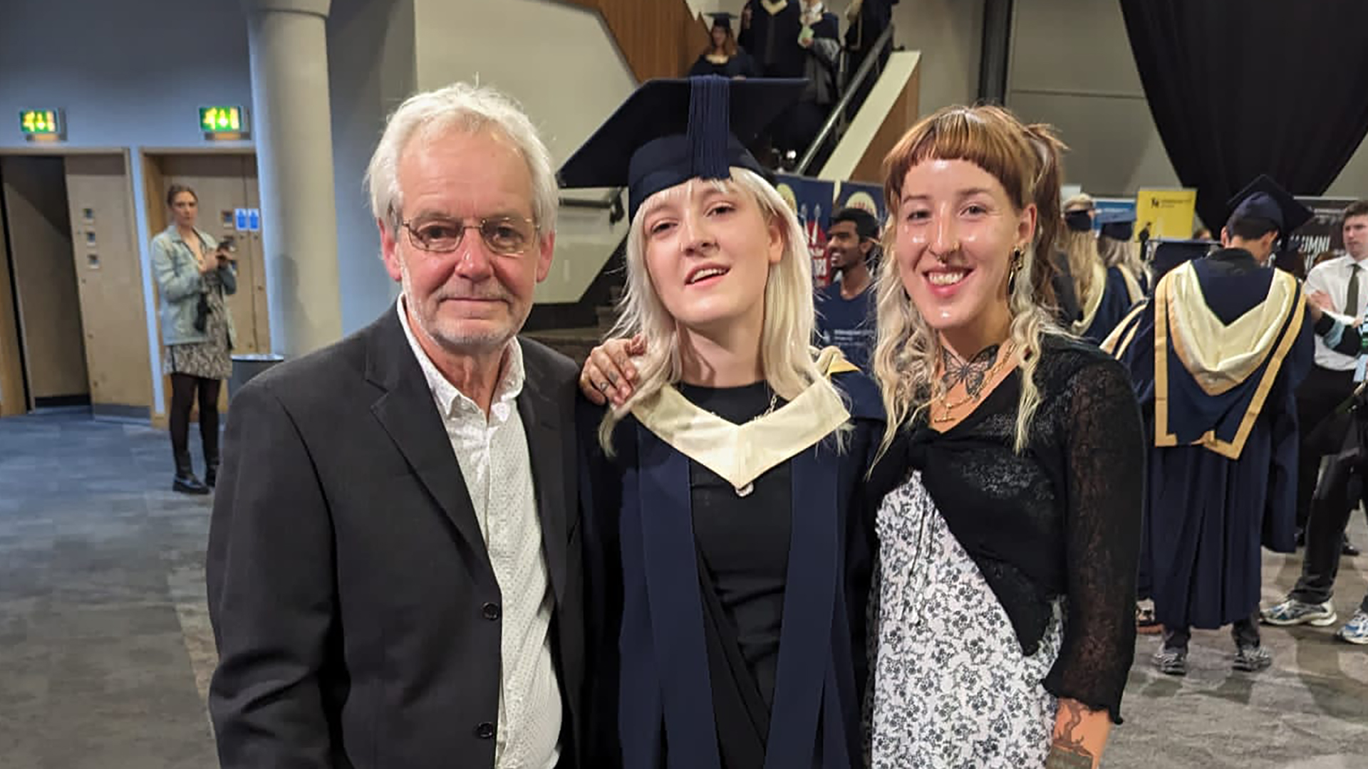A man with his two daughters, the middle one is wearing graduate robes
