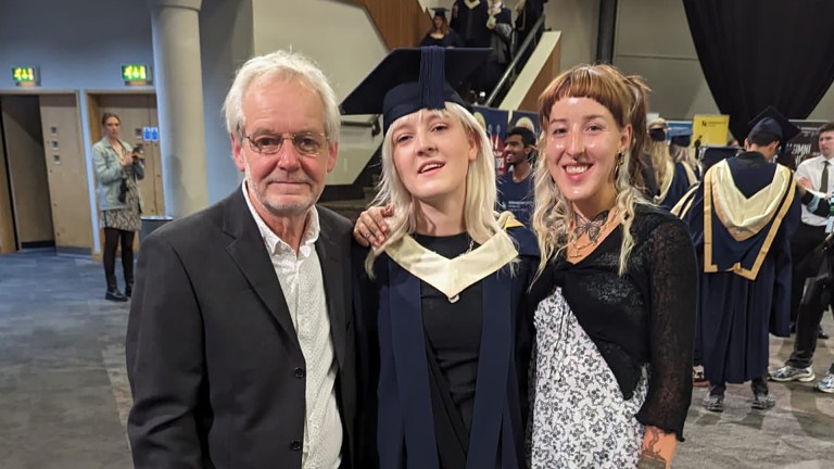 A man with his two daughters, the middle one is wearing graduate robes