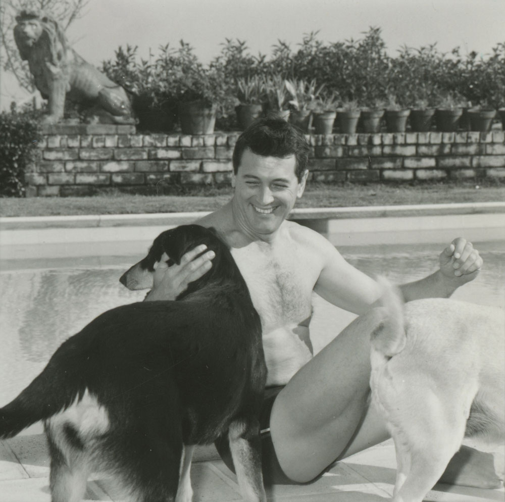 Rock Hudson smiling with a dog, beside a pool