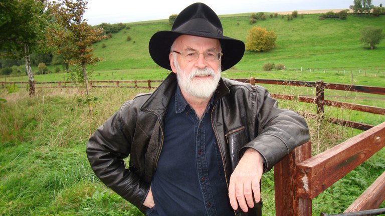 Terry Pratchett standing in a field, wearing a black hat