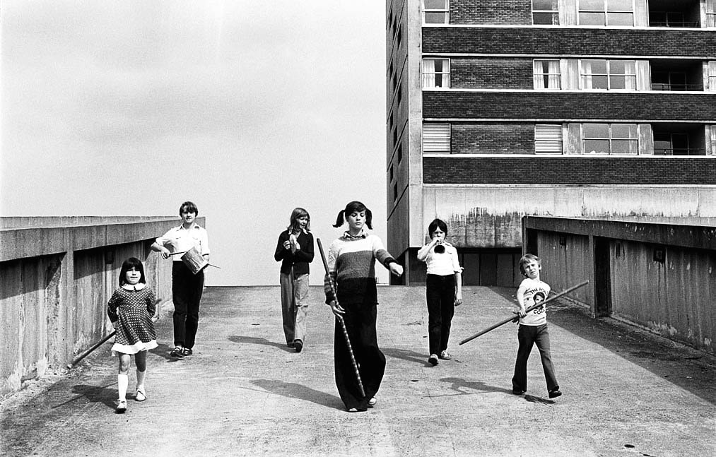 Black and white: six kids carrying instruments walk through a housing estate