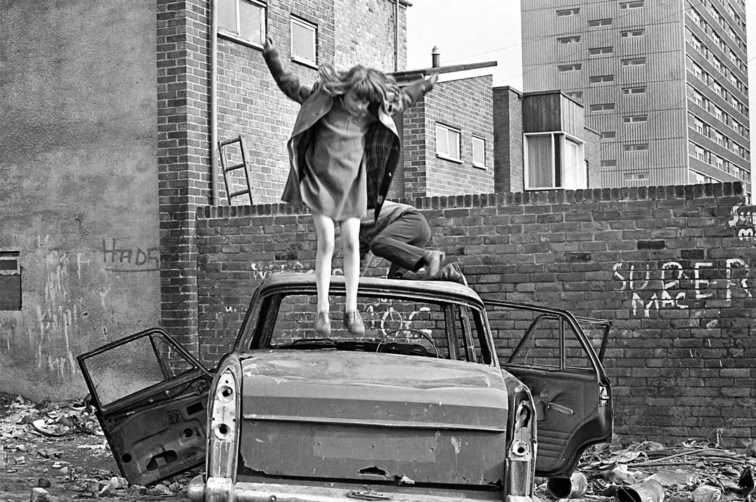 Black and white: a young girl jumps on an abandoned car