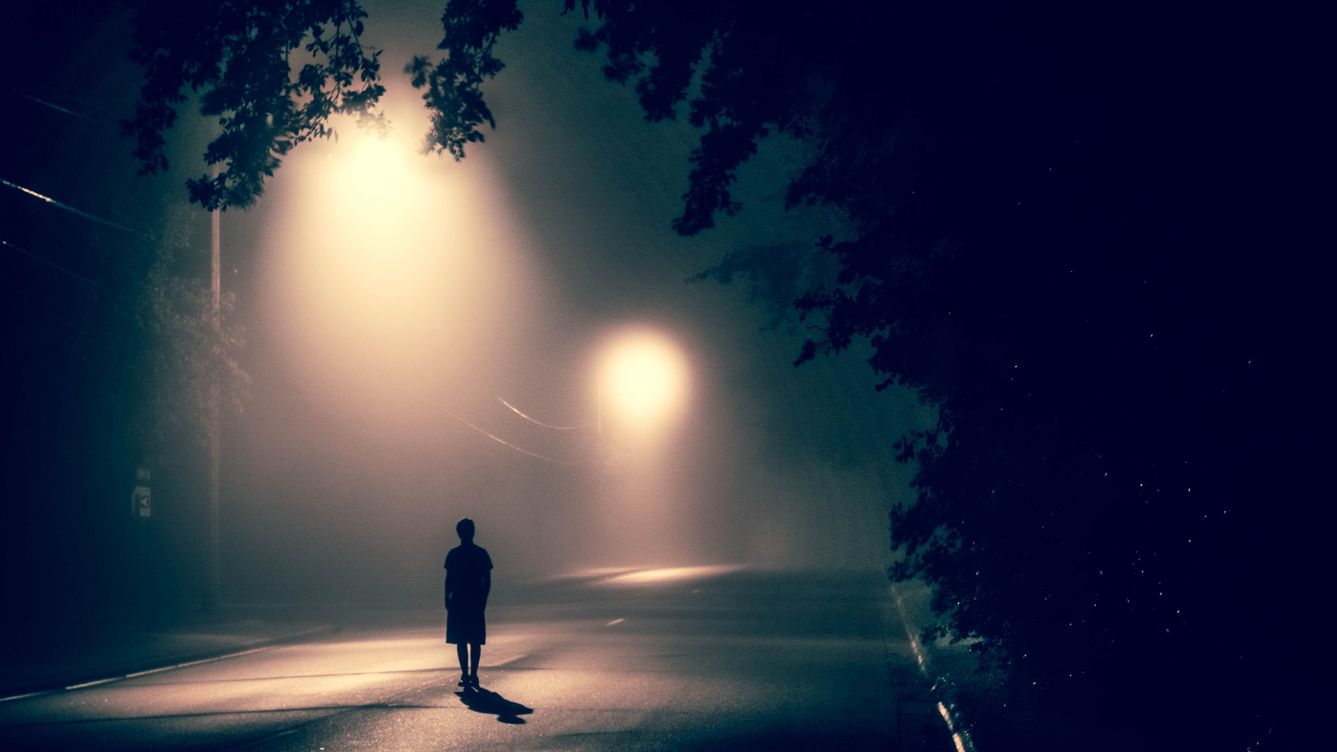 A young person in silhouette on a dark, misty road