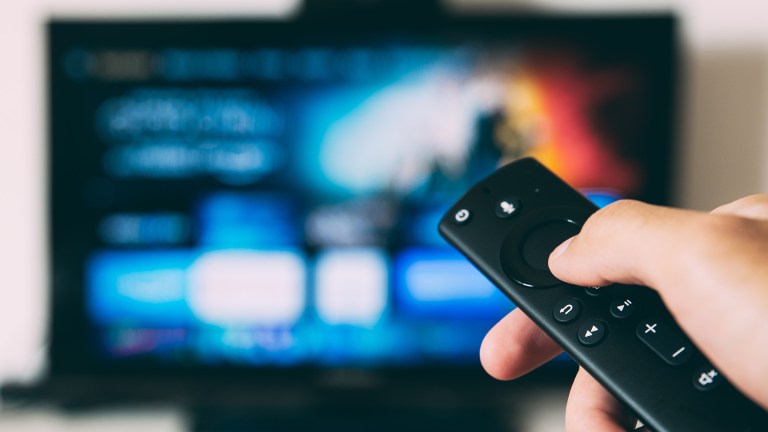 A hand pointing a tv remote at a screen
