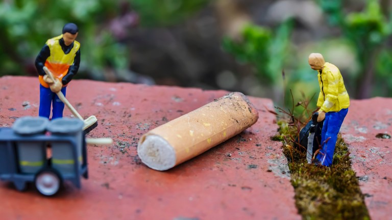 Tiny models of bin men cleaning up a giant cigarette butt