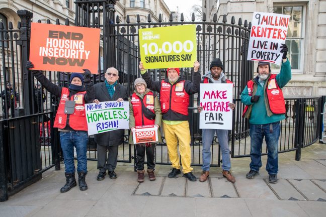 A group of Big Issue vendors and campaigners and Lord Bird standing outside the gates of Downing Street with placards calling for an end to housing insecurity