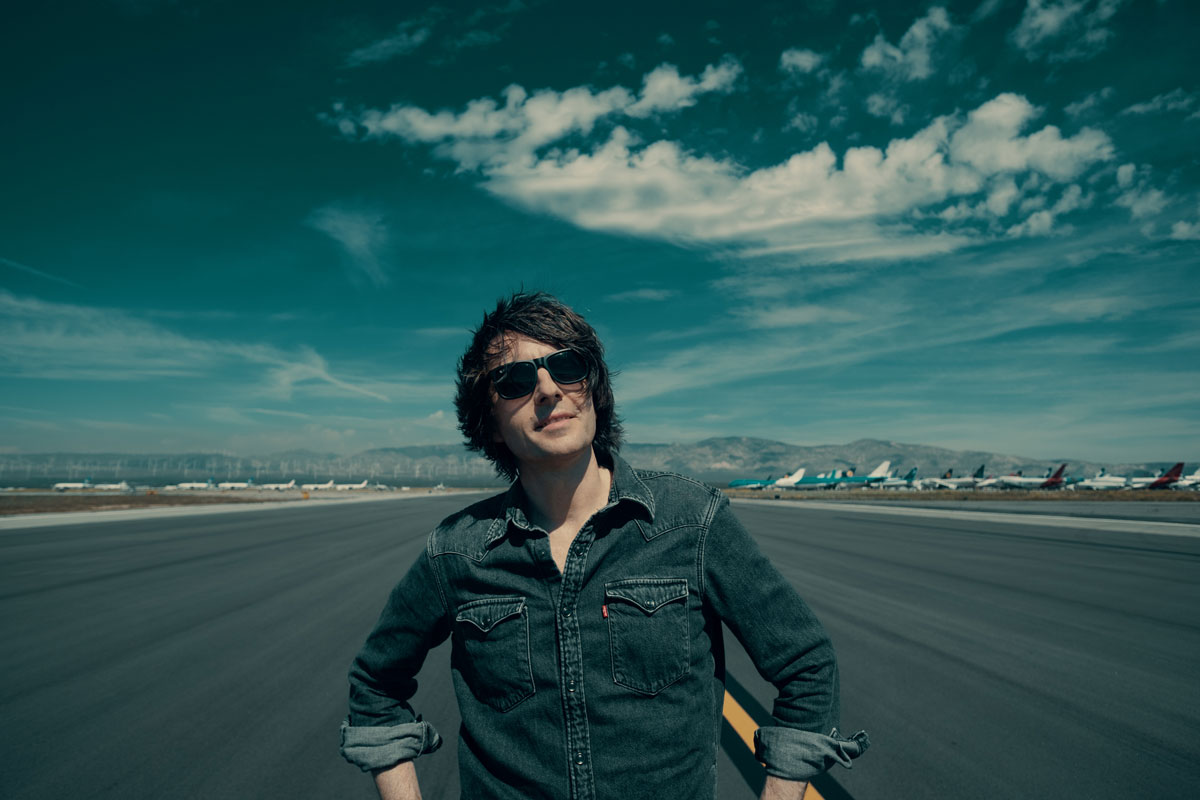 Danny Robins wearing sunglasses on a runway in front of planes
