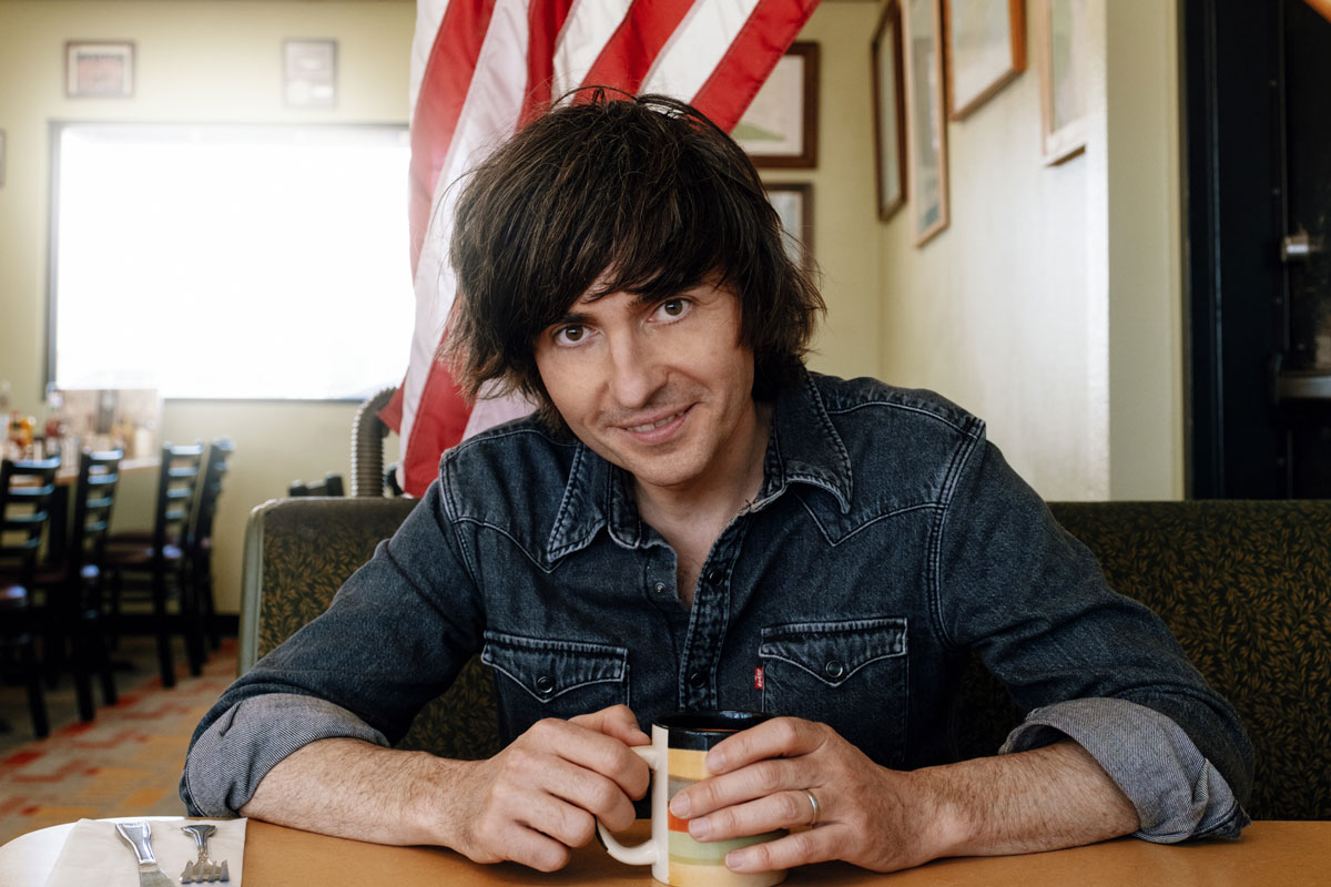 Danny Robins in front on an American flag in a diner for Uncanny USA