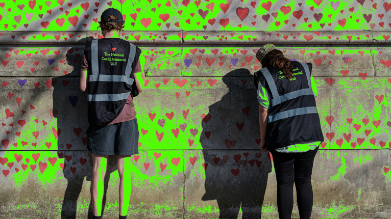 Two people in vests work on the Covid memorial wall