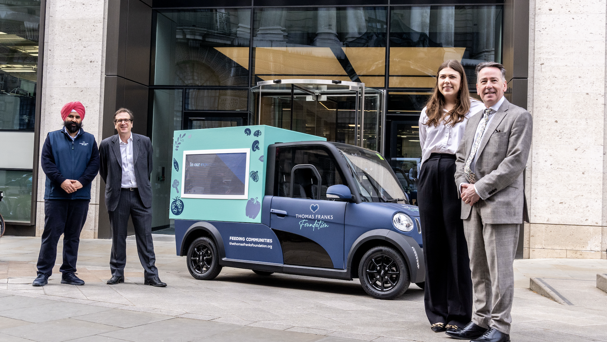 Four people stand around an electric van