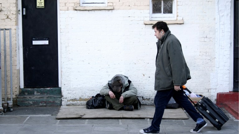 a man with a suitcase walking past a man sleeping rough