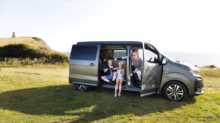 Vicky Parrott and her daughters Flo and friend Evie enjoying the spacious interior of the Citroën Holidays camper van during their Dorset coast family day trip, with sliding doors open and sea views in the background