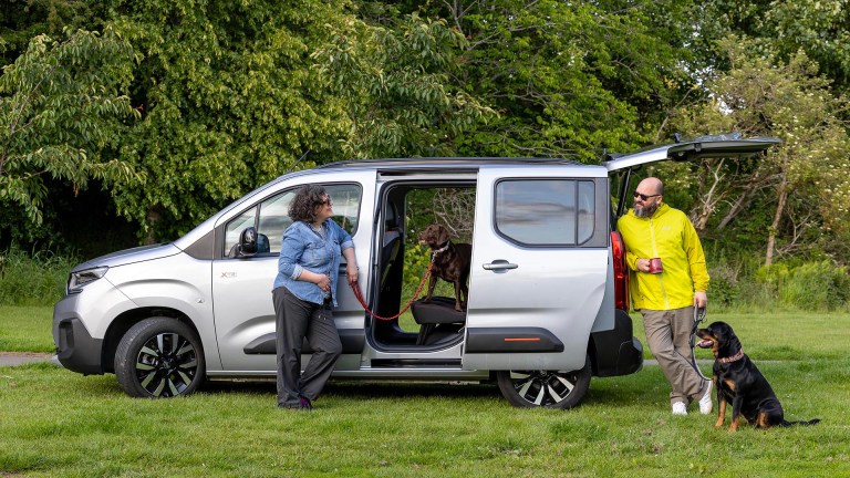 Couple with dogs standing beside silver Citroën ë-Berlingo with sliding doors open showing spacious interior