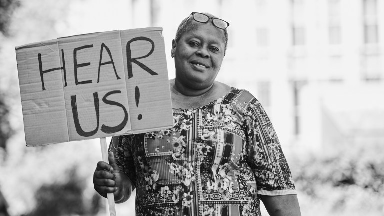 A woman holding up a sign saying 'HEAR US'