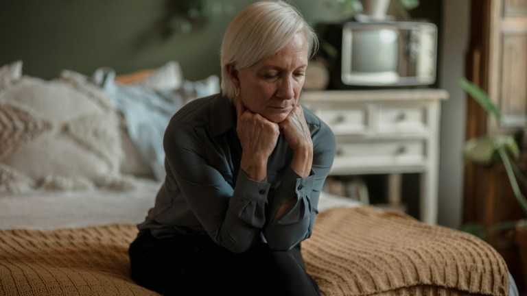 an old woman sat on a bed looking stressed