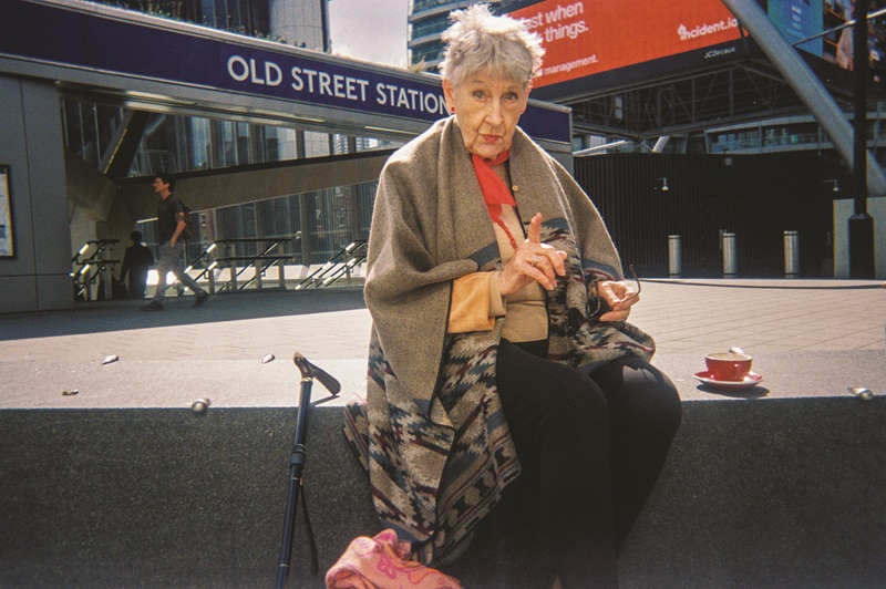 Old woman sat on step outside London 's Old Street Station