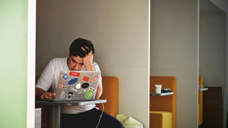 Photo shows a man working on a laptop with his head in one hand