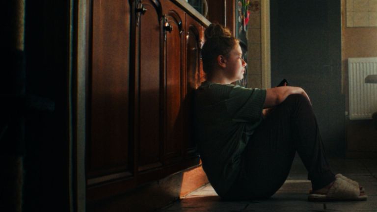 Screenshot of the film More Than A Parent depicts an unpaid parent carer sitting on the floor of her kitchen