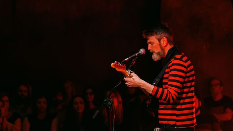 Photo shows musician Rodney Owl singing and playing guitar on stage