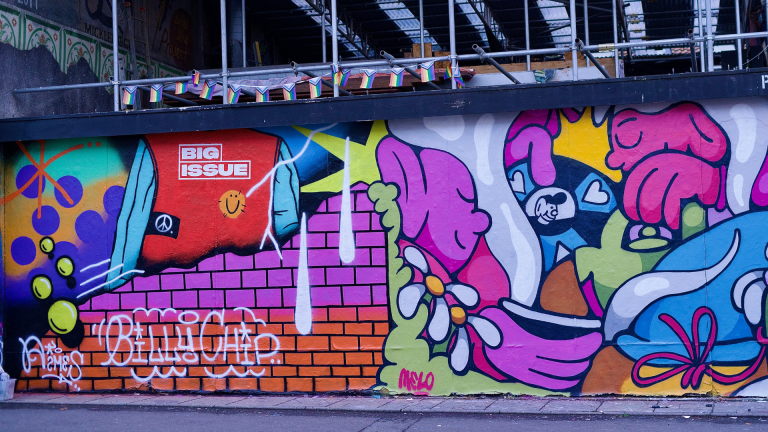 A Big Issue vendor tabard is featured as one of several graffiti art pieces brought together on a city wall.