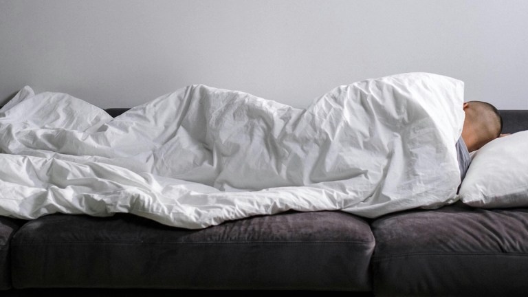 A person sleeping on a sofa wrapped in a duvet