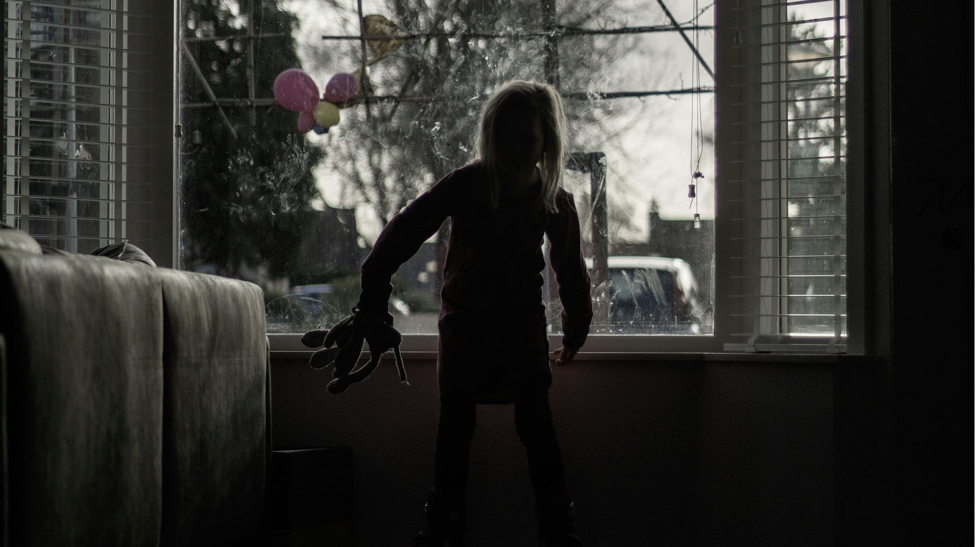 a girl in the front room of a home in front of the window