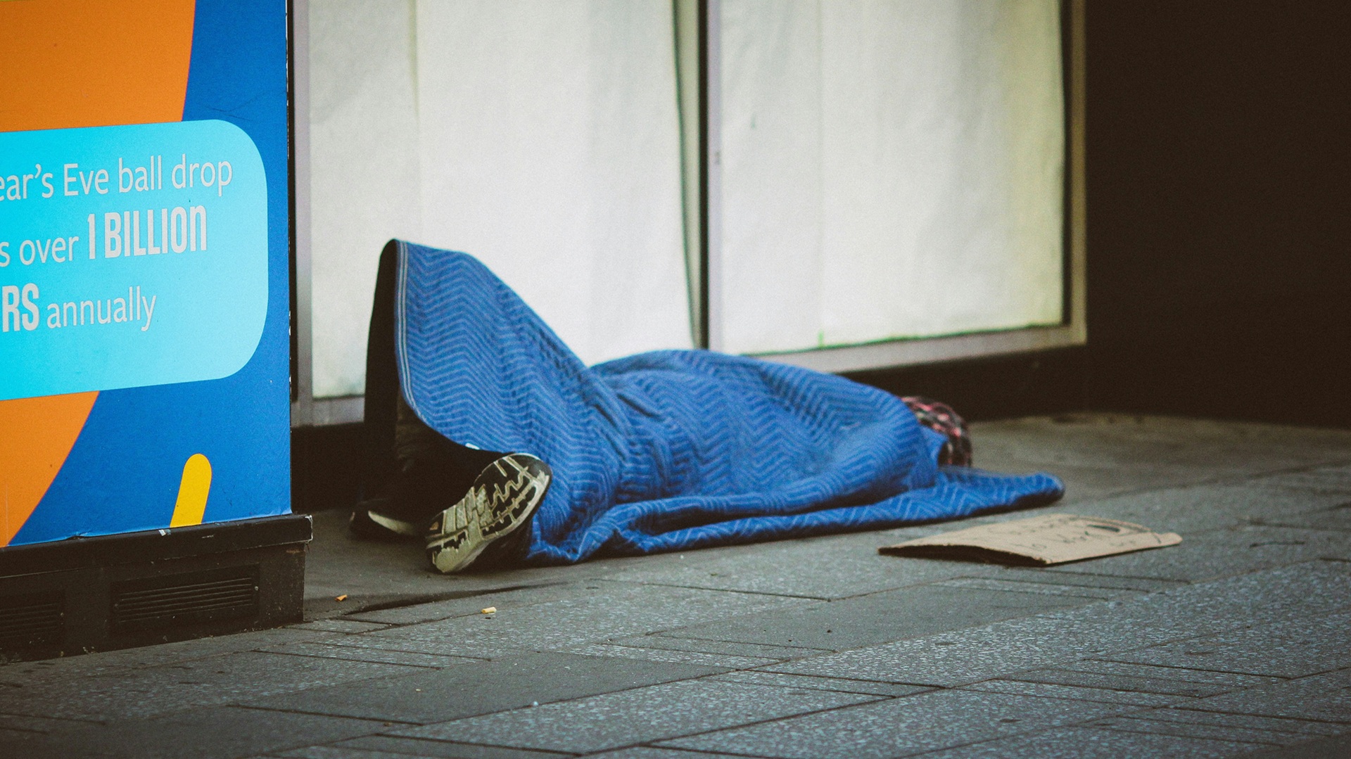 a person rough sleeping under a blue blanket on the street