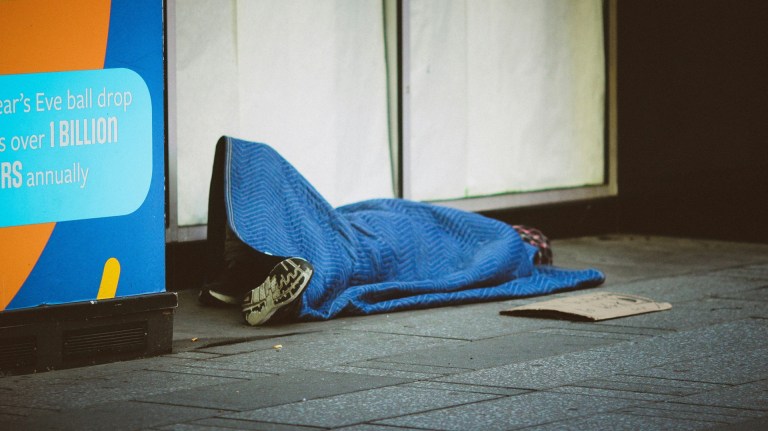 a person rough sleeping under a blue blanket on the street