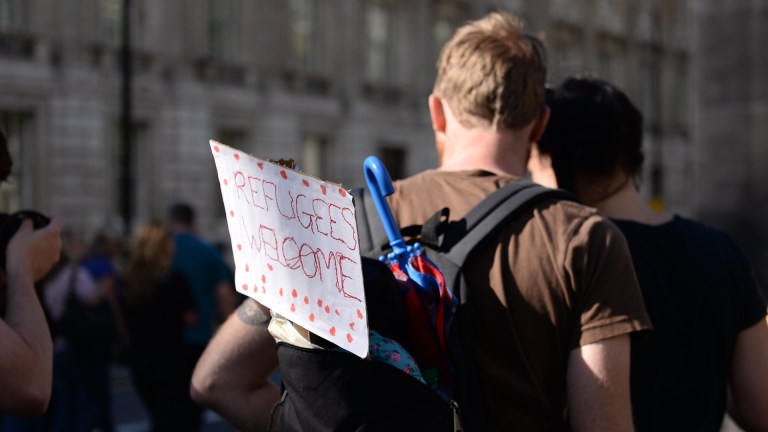 a man with a Refugees Welcome sign in his backpack