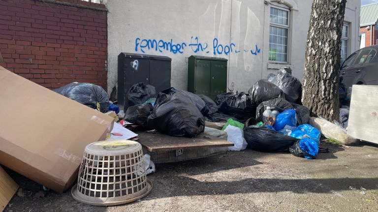 rubbish lines the streets in Birmingham with graffiti saying 'remember the poor' on a wall