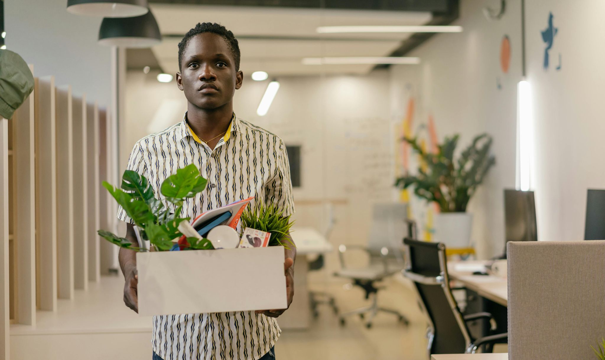 Stock image of a man walking out of an office with his belongings after being made redundant