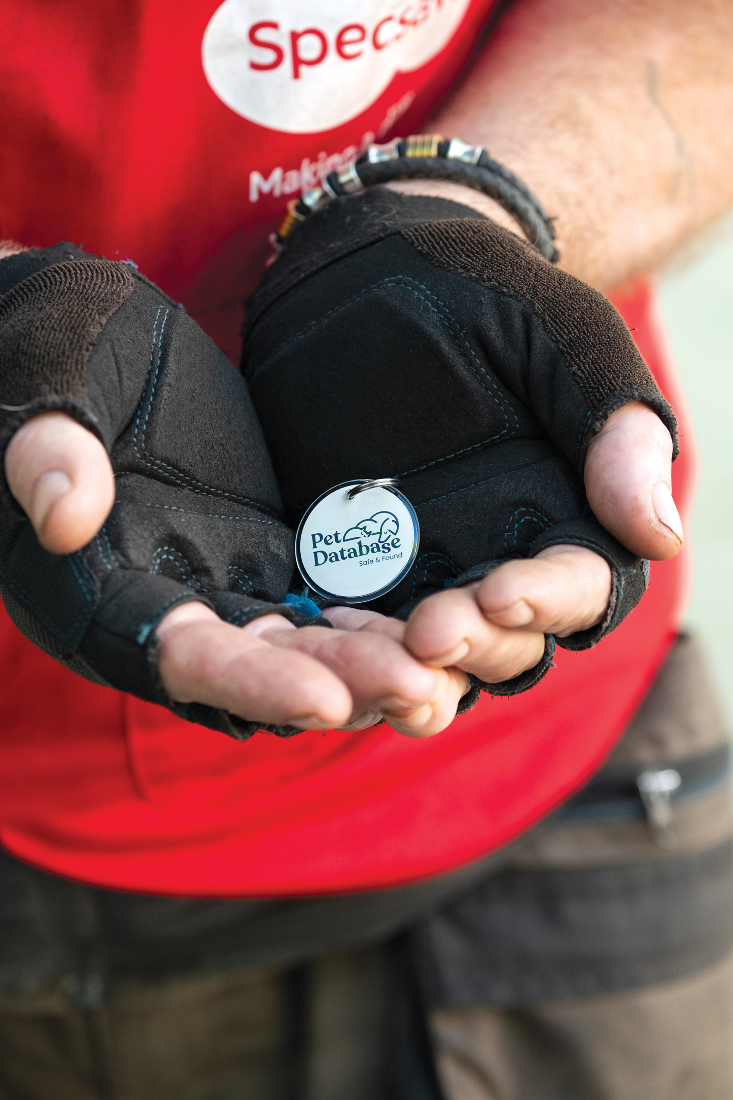     Close-up of a Pet Database smart pet tag resting in the hands of Big Issue vendor Clive Rowe, showing the round QR-enabled pet ID tag used to help reunite lost pets with their owners.